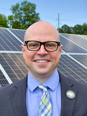 Person with glasses, smiling at the camera, wearing a shirt and tie
